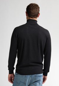 Schwarzer Wollrollkragensweater mit einem enganliegenden Schnitt, geripptem Kragen und Bündchen. Kombiniert mit blauen Denim-Jeans mit dezenten Nähdetails.