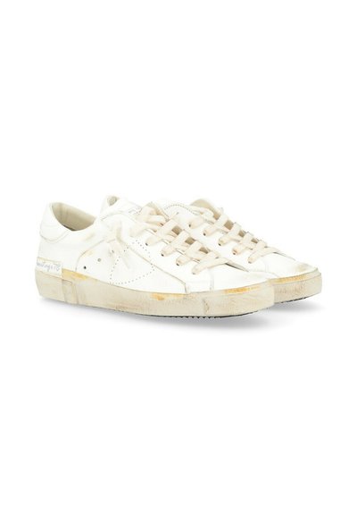 Sneakers bianchi in pelle con chiusura a lacci, superficie testurizzata e suola consumata. Presentano cuciture sottili e un logo sul lato.