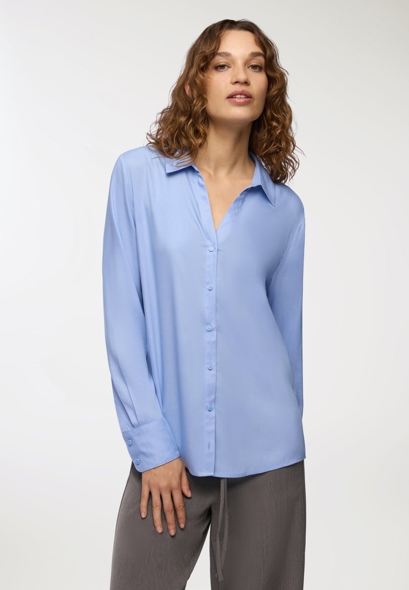 Jasnoniebieska koszula zapinana na guziki, wykonana z gładkiego materiału, z wykładanym kołnierzykiem, długimi rękawami z mankietami zapinanymi na guziki oraz luźnym krojem.