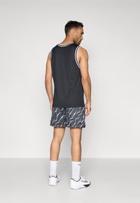 Μαύρο αμάνικο μπλουζάκι με λευκή περιγραφή, συνδυασμένο με μοτίβο σορτς σε αποχρώσεις του γκρι, λευκές αθλητικές κάλτσες και λευκά αθλητικά παπούτσια.