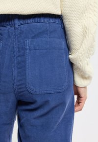 Pantalon en velours côtelé bleu avec une taille élastique et deux poches arrière, présentant une fine texture côtelée et des coutures détaillées.