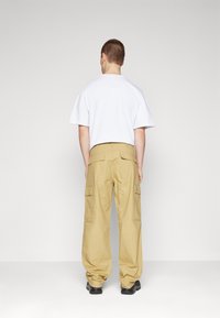 Beige cargo bukser med flere lommer, en løs pasform og en blød tekstur. Sammen med en kortærmet hvid t-shirt. Sorte sko.
