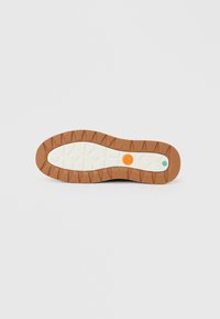 Dambas kurpes zole ar strukturētu brūnu ārpusi, gaišas krāsas vidējo zoli un izteiktām apļu un sešstūra akcentu detaļām oranžā un zaļā krāsā.