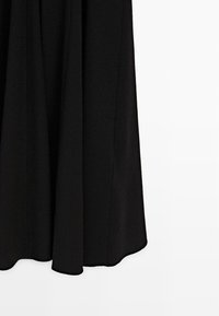 Černý látkový závěs s jemnými vertikálními záhyby visící na bílém pozadí.