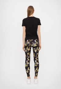 Juoda trumpa rankovė marškiniai derinami su prie kūno priglundančiomis tamprėmis, puoštomis geltonų ir baltų gėlių raštu ant juodo fono. Baltos sportbačiai.