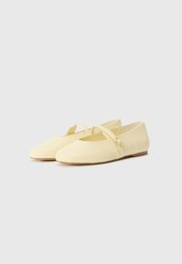 Ballerines jaunes à bout rond, avec une bride sur le pied et une petite boucle décorative. Tige en cuir lisse et semelle plate.