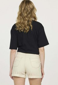 T-shirt noir à manches courtes associé à un short beige clair avec ourlet retroussé. Le tissu semble lisse avec des détails de couture visibles sur le short.