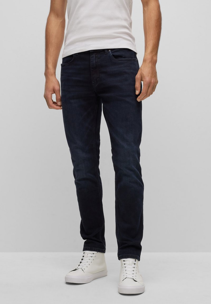 Tmavě modré džíny s slim fit střihem, které mají pět kapes, zipový klín a jemné blednutí. S kombinací bílých sneakerů s vysokým střihem.