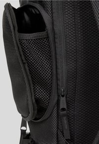 Musta reppu, jossa on teksturoitu ulkopinta, verkkomaiset sivutaskut ja sileät vetoketjuominaisuudet turvallista säilytystä varten. Kestävä kangas jokapäiväiseen käyttöön.