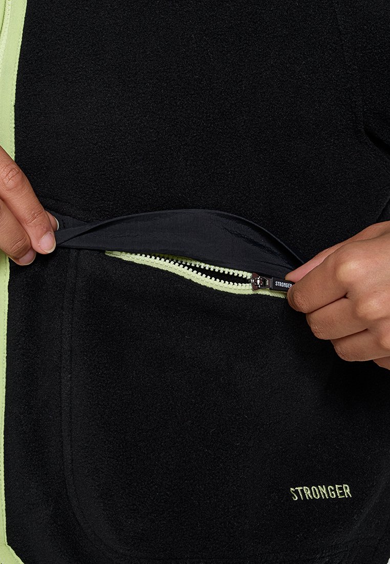 Schwarze Fleecejacke mit einer gelben Reißverschlusstasche auf der linken Seite und einem gestickten "STRONGER"-Logo in Gelb nahe dem Saum.