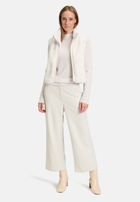 Kamizelka z sztucznego futra w kolorze białym na lekkim swetrze, zestawiona z szerokimi spodniami w kremowym kolorze i beżowymi botkami za kostkę. Miękka tekstura, nowoczesny design.