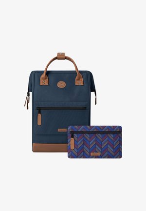 Sininen kangaskassi, jossa on ruskeita yksityiskohtia, etutasku ja irroitettava kuvioitu pussukka, jossa on purppura- ja sinikehyksinen chevron-muotoilu.