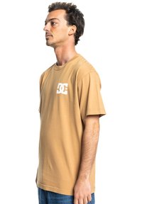 Brown cotton t-shirt with short sleeves, featuring a white logo on the left chest. Straight-cut hem, soft texture, and relaxed fit.