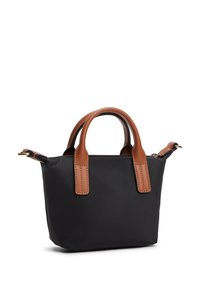 Μικρή μαύρη τσάντα χειρός με καφέ δερμάτινες λαβές και αποσπώμενο ιμάντα ώμου, απλός σχεδιασμός, που στέκεται σε λευκό φόντο.