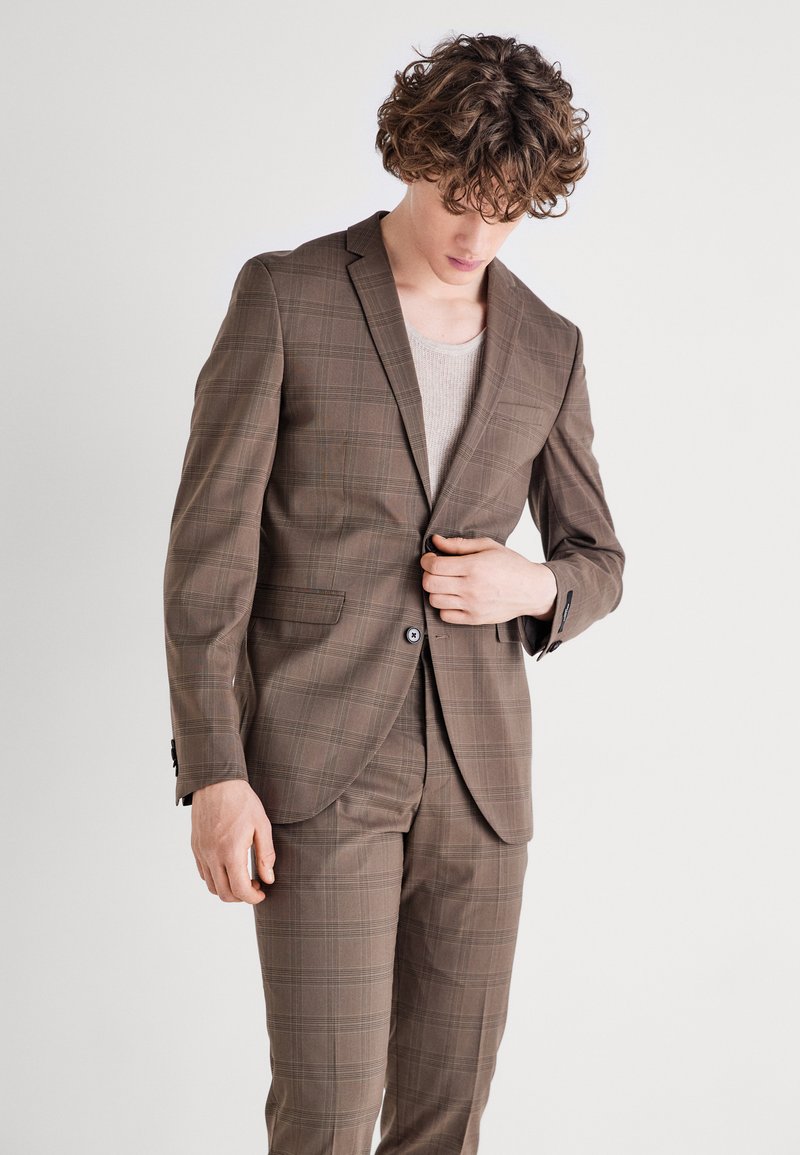 Costum cu carouri maro, format din sacou cu două butoane și pantaloni asortați. Țesătura are o textură netedă, cu detalii subtile ale modelului și cusături contrastante.
