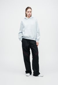 Jasnoniebieska bluza z kapturem z kieszonką z przodu, w połączeniu z czarnymi spodniami dresowymi z czerwonymi detalami. Model nosi białe obuwie.