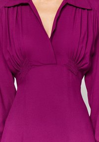 Magenta omlottklänning med långa ärmar, med gathered detaljer vid midjan och en djup V-halsdesign. Slät textur, figurn ära siluett.