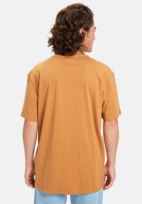 Short-sleeve, relaxed-fit t-shirt in warm brown cotton, featuring a round neckline and smooth texture, with a straight hem and no graphics.