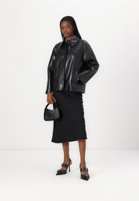 Giubbotto di pelle nera con design a colletto e vestibilità ampia, abbinato a una gonna midi nera, una piccola borsa nera e scarpe col tacco a punta.
