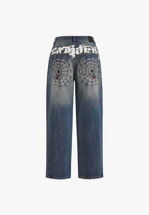 Donkerblauwe denim jeans met een ontspannen pasvorm, voorzien van witte spinnenwebborduring op de achterzakken en een opvallend logo erboven.