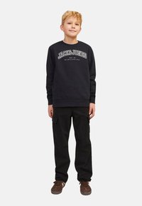 Czarna bluza z białym napisem "JACK & JONES", w zestawieniu z czarnymi spodniami cargo z kieszeniami. Brązowe sneakersy dopełniają stylizację.