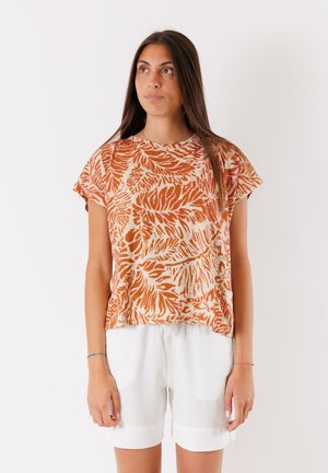Top a maniche corte, arancione e beige a fantasia con scollo rotondo, realizzato in tessuto leggero, abbinato a pantaloni corti bianchi per un contrasto.