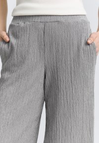 Pantalones amplios gris de pliegues con un acabado texturizado, cinturilla elástica y bolsillos laterales, con un patrón de rayas vertical.