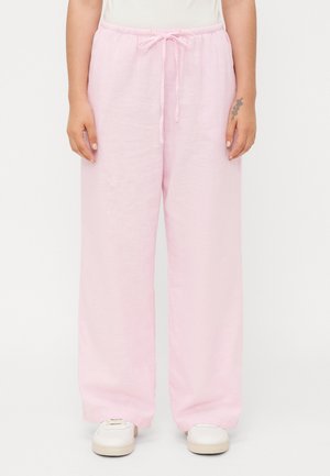 Person wearing light pink wide-leg pants with a drawstring waist and white sneakers, standing against a plain background.