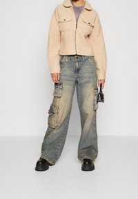 Beige fleece zip-jakke med to brystlommer, parret med oversized blå denim cargo bukser med baglommer og en tapered ben. Sorte platform støvler.