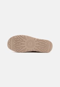 Schuhsohle aus weichem beigen Gummi, mit einem strukturierten Zickzackmuster für besseren Halt, einer gerundeten Vorderseite und einem sonnenähnlichen Emblem in der Mitte.