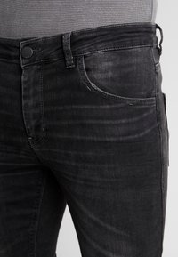 Jeans de mezclilla negra con un ligero desgaste, diseño de cinco bolsillos y cierre de botón. Presentan una textura suave y un corte estándar.