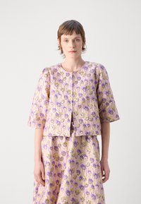 Kortermet rosa jakke med blomsterdesign i lilla og grønt, med rund hals og åpning foran. Glatt, teksturert stoff.