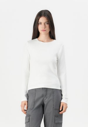 White long-sleeve fitted top made of smooth fabric with a round neckline, paired with gray cargo pants featuring side pockets and visible stitching.