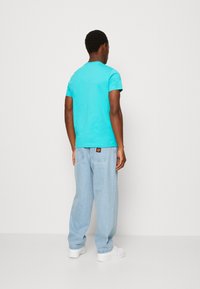 Turquoise cotton t-shirt with short sleeves, paired with light blue baggy jeans and white sneakers, viewed from the back.
