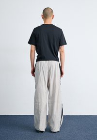 Černé bavlněné tričko a šedé lehké kalhoty širokých nohavic s černými bočními detaily. Minimalistický design s volným střihem, pohled zezadu.