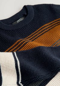 Granatowy sweter z dzianiny o teksturowanej powierzchni; ma pomarańczowe i szare paski; okrągły dekolt; miękki, gruby materiał; widoczna metka.