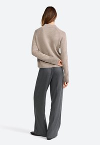 Maglione beige a maglia con polsini e orlo a coste, abbinato a pantaloni grigi a gamba larga. L'ensemble ha una vestibilità rilassata e confortevole.