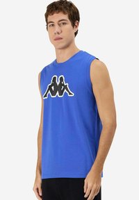 Maglietta senza maniche blu in cotone con scollo rotondo. Presenta un logo grafico nero di due figure centrato sul petto.