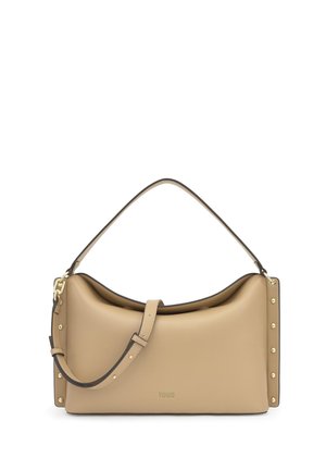 Bolso de cuero beige con correa ajustable, tachuelas doradas en los lados y logotipo "TOUS" en relieve en el centro frontal.