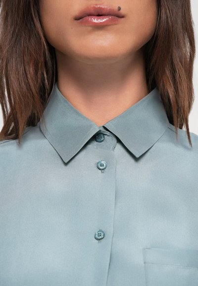 Light blue satin shirt with a collar, featuring two buttons and a chest pocket. Smooth texture with a subtle sheen, minimalistic design.
