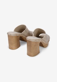 Zuecos beige de espalda abierta con tacón plataforma. Material suave con tachuelas doradas a lo largo del borde y una base de madera texturizada.