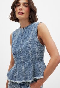 Lichtblauwe denim peplum top met een gestructureerde afwerking. Beschikt over een ronde halslijn en een rafelige zoom. Mouwloos ontwerp met een aansluitende bustehouder.