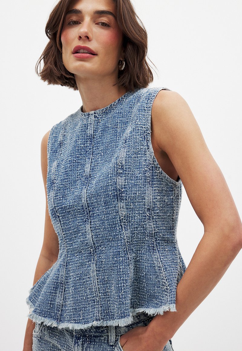 Lichtblauwe denim peplum top met een gestructureerde afwerking. Beschikt over een ronde halslijn en een rafelige zoom. Mouwloos ontwerp met een aansluitende bustehouder.