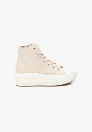 Zapatilla beige de caña alta con suela gruesa de goma blanca, puntera redonda, cordones y un parche circular con el logo en el lateral del tobillo.
