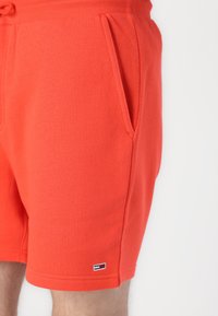 Pantaloni corti rossi di cotone con vita elastica, tasche laterali e una piccola etichetta con logo sull'orlo. Tessuto liscio, design fino al ginocchio.