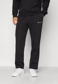 Pantalons de survêtement en polaire noire avec une taille élastique, poches latérales ouvertes et un logo brodé blanc sur le côté gauche.