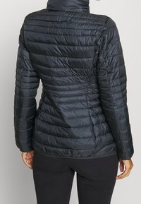 Giacca a vento nera con texture trapuntata, collo alto e sagoma aderente. Il materiale sembra liscio e leggero con cuciture orizzontali.