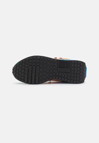 Semelle de basket Puma, en caoutchouc noir avec des cercles texturés, arborant le logo de la marque et des accents striés, avec des bandes colorées en bleu, vert et orange.