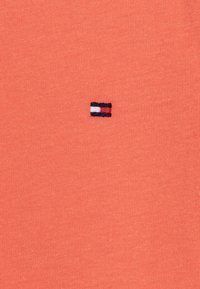 Koralfarvet t-shirt lavet af blødt bomuld. Har et lille broderet logo med røde, hvide og blå striber på brystet. Glat tekstur.