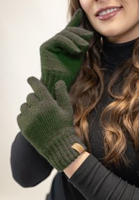Zelené pletené rukavice s žebrovanou strukturou a koženou značkovou nášivkou. Design se vyznačuje těsným střihem u zápěstí a mírně špičatými prsty.
